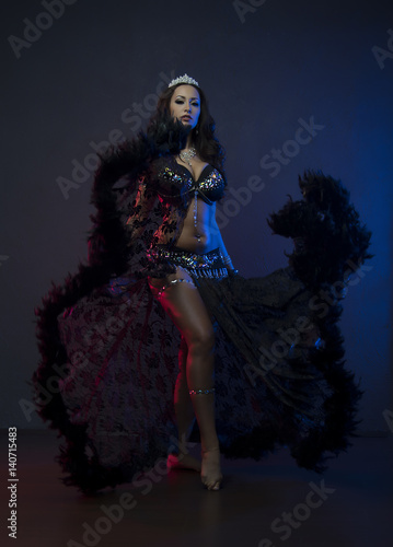 Sexy slim woman, belly dancer in black costume with crystals. Dark background with pink and blue lightening