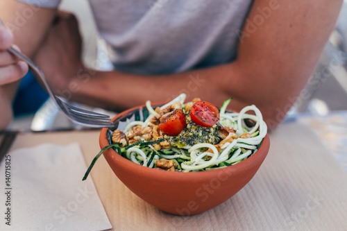 Young man eats a vegan zoodles with pesto and vegetables