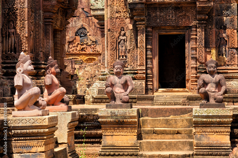 Fototapeta premium Banteay Srei temple, Angkor, Cambodia. Statues of human figures with animal heads, guardians at the ancient Khmer temple built in red sandstone
