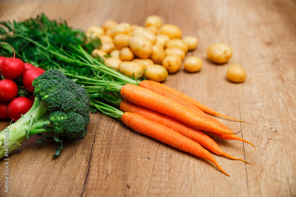Potatoes with carrot. Red radish, brocoli and raw new potato. Fresh natural vegetables. Organic bio food. On wooden table. Potatoes with carrot. Red radish, brocoli and raw new potato. Fresh natural vegetables. Organic bio food. On wooden table.