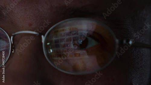 Surfing internet with screen reflection in glasses. Man in glasses is surfing web internet in a dark room. Closeup candid face shot.