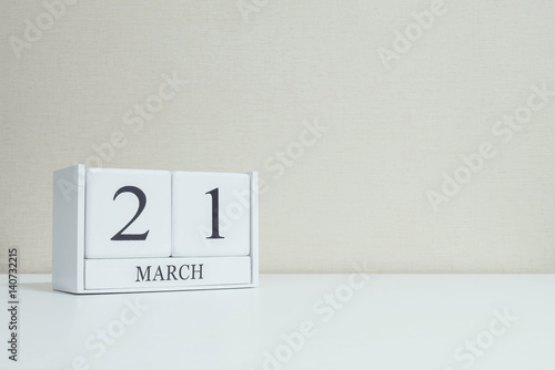 Closeup white wooden calendar with black 21 march word on blurred white wood desk and cream color wallpaper in room textured background with copy space , selective focus at the calendar