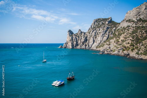View of the Bay, cliffs, ships and yachts on the waves of the blue sea. Rocky Cove with calm water in foreground and mountains and cliffs in the background.