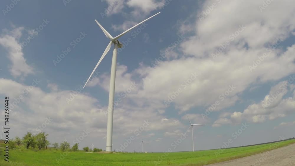 Working wind power station in a green field with blue sky and clouds Working wind power station in a green field with blue sky and clouds