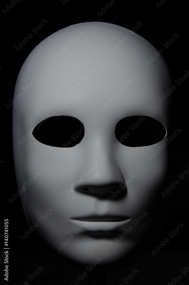 White mask with neutral expression and shadows on dark background White mask with neutral expression and shadows on dark background
