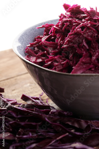 Shredded red cabbage in clay bowl on wooden background. Vegetari