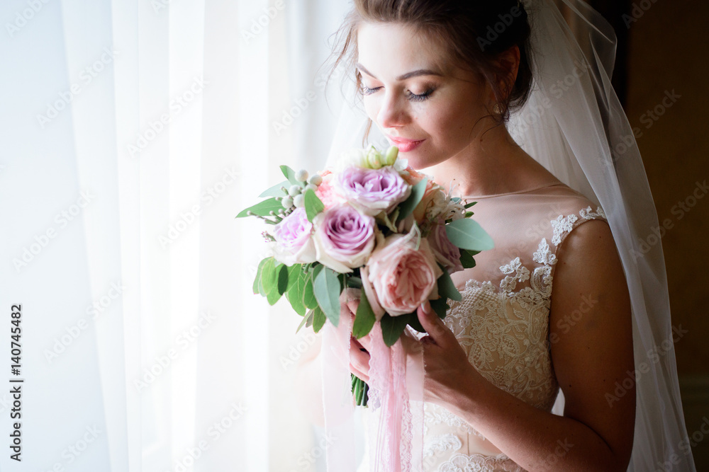 Beautiful bride holds violet and pink wedding bouquet before her face Beautiful bride holds violet and pink wedding bouquet before her face