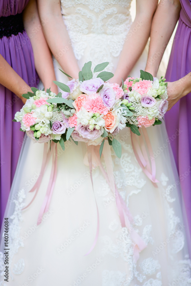 Bride and bridesmaids in violet dresses hold together tender wedding bouquets Bride and bridesmaids in violet dresses hold together tender wedding bouquets