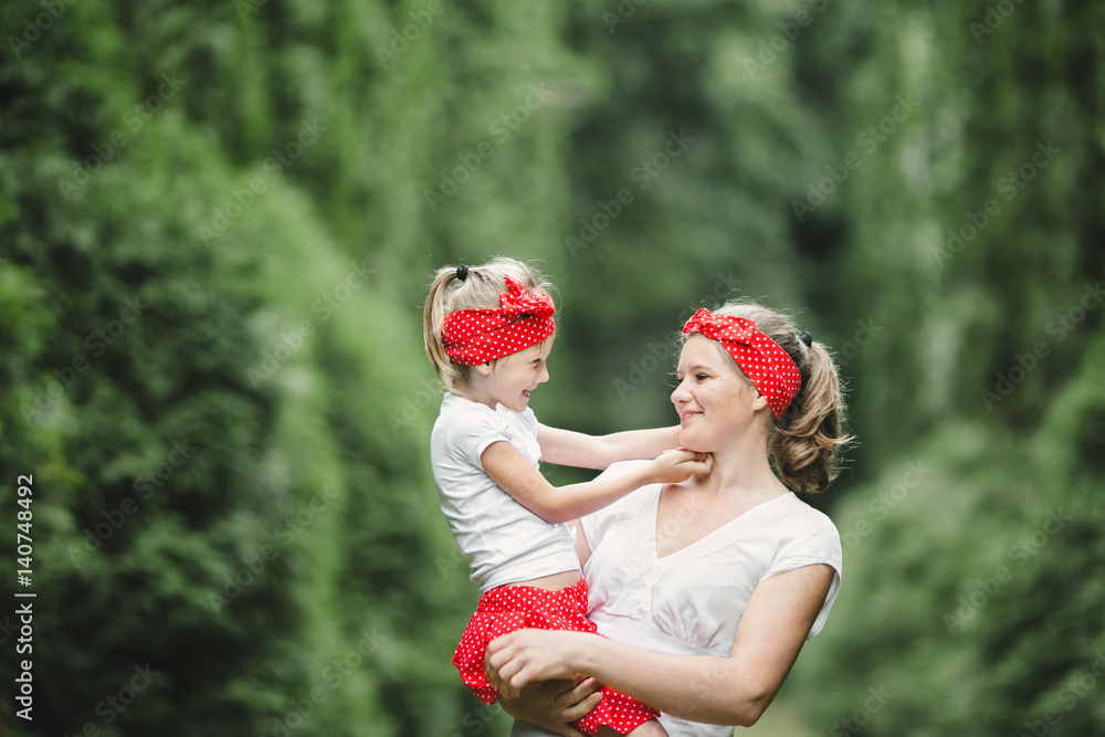 Obraz premium Girl touches mother's hands tender while they stand among tall green trees