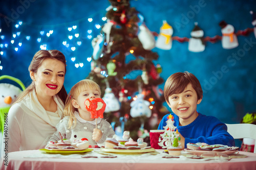 Smiling little boy sits with his mother and sister at dinner table in room with Christmas tree