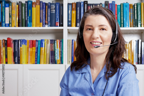 Billede på lærred Friendly smiling woman with headset talking to a customer during a video call, webcam view, copy space