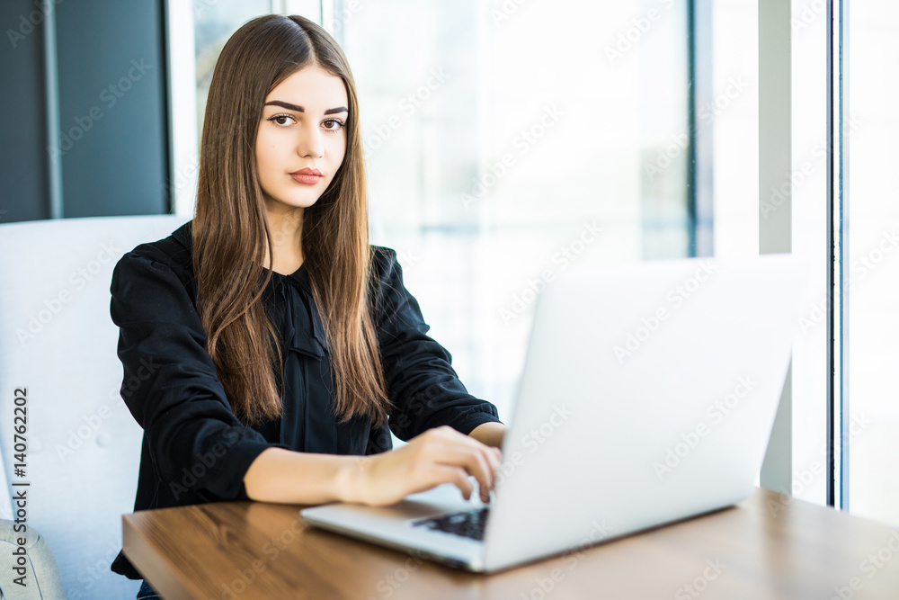 Beautiful young woman working at the laptop and looking at camera in cafe Beautiful young woman working at the laptop and looking at camera in cafe