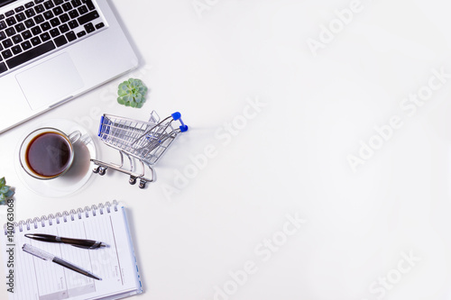 On-line shopping concept - lapytop keyboard, shopping cart and coffee, copy space on white table background