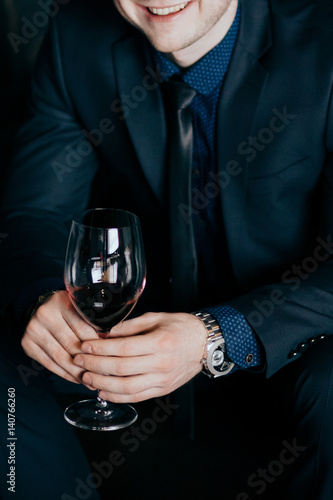 successful man keeps watch and clothes With a glass of red wine