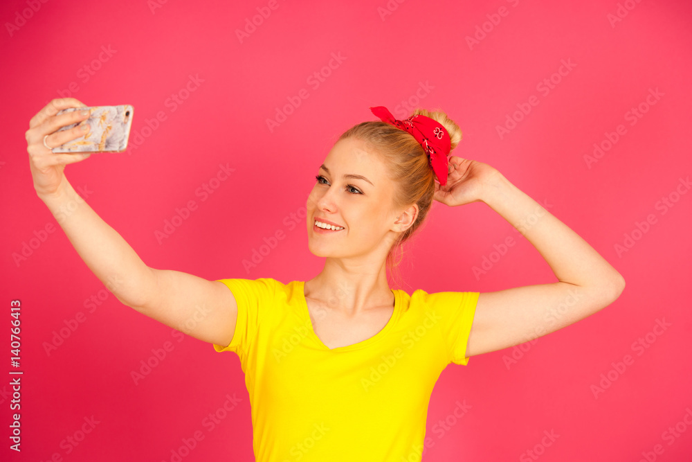 Beautiful young blond teenage woman in yellow t shirt taking selfie over pink background. Beautiful young blond teenage woman in yellow t shirt taking selfie over pink background.