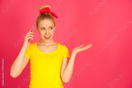cut teenage woman in yellow t shirt talks on smart phone over pink bacckground