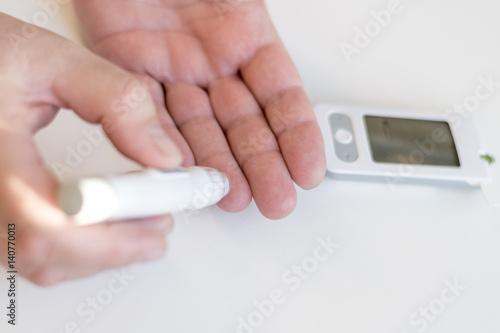 Medicine, diabetes, glycemia, health care and people concept - Close up of man hands using lancet on finger to check high blood sugar level with glucometer or glucose meter at home