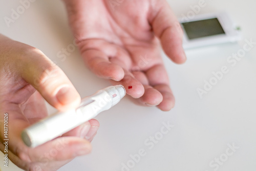 Medicine, diabetes, glycemia, health care and people concept - Close up of man hands using lancet on finger to check high blood sugar level with glucometer or glucose meter at home