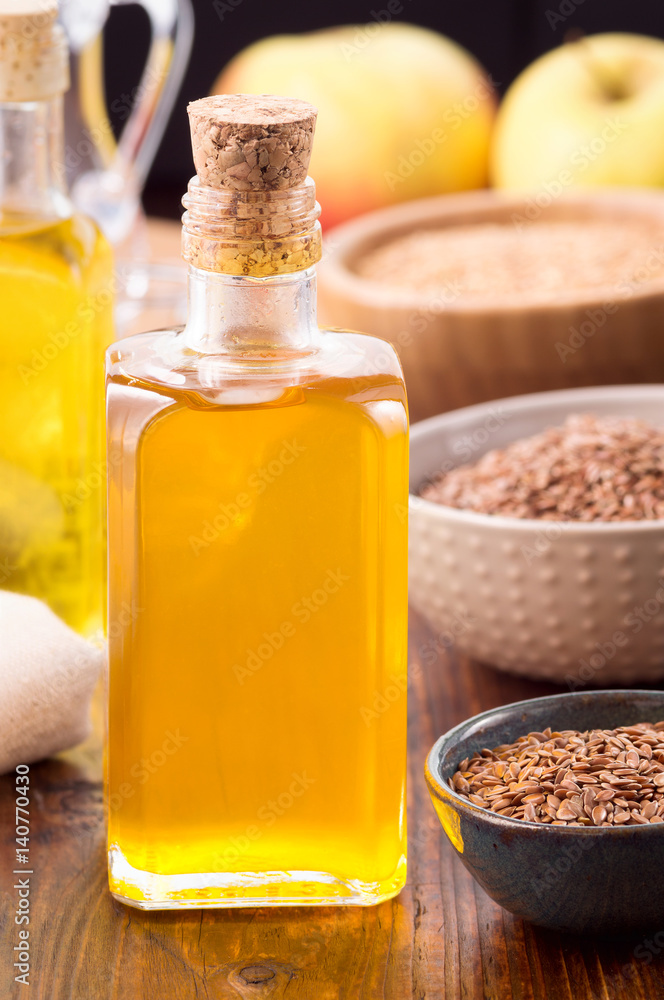 Nonrefined flaxseed oil in a bottle and brown flax seeds in bowl on wooden table. Vertical shot Nonrefined flaxseed oil in a bottle and brown flax seeds in bowl on wooden table. Vertical shot