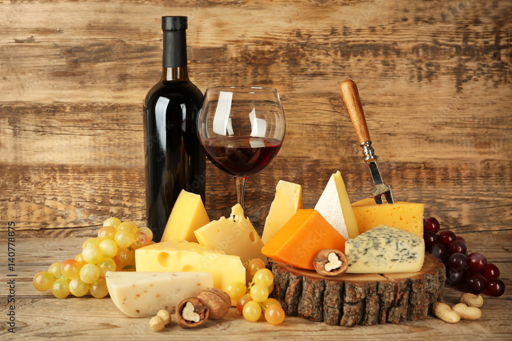 Naklejka premium Red wine and stump with variety of cheese on wooden background