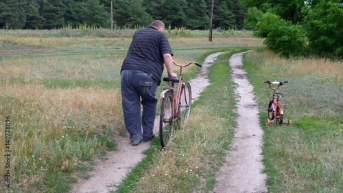 Fat senior man walks on a country road with an old broken bicycle and found the kids tricycle he likes