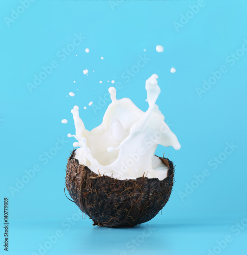 Cracked coconut with splashes of milk on color background
