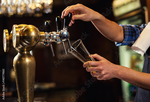 Bartender pouring the fresh beer in pub,barman hand at beer tap pouring a draught lager beer,beer from the tap,Filling glass with beer,fresh beer,pub.Bar.Restaurant.European bar.American bar.