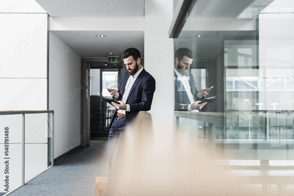 Businessman standing in office building, using smart phone and digital tablet Businessman standing in office building, using smart phone and digital tablet
