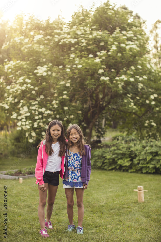 Portrait of happy sisters standing on grass in back yard Portrait of happy sisters standing on grass in back yard
