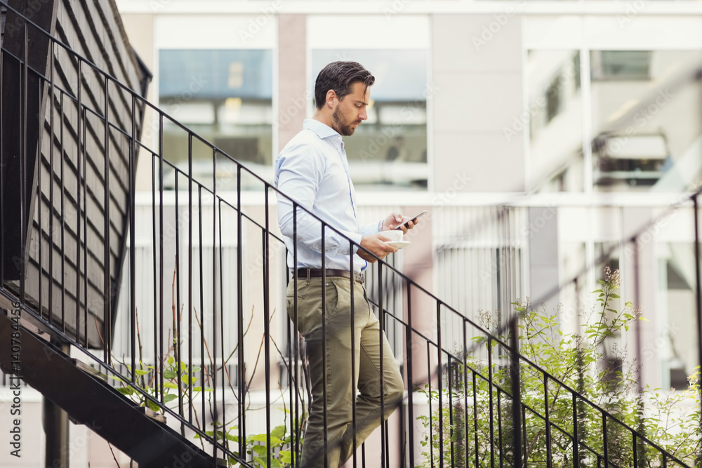 Side view of businessman using smart phone while moving down steps of log cabin Side view of businessman using smart phone while moving down steps of log cabin