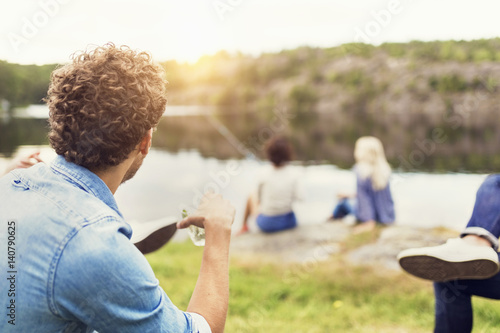 Men having drink while female friends fishing at lakeshore photo