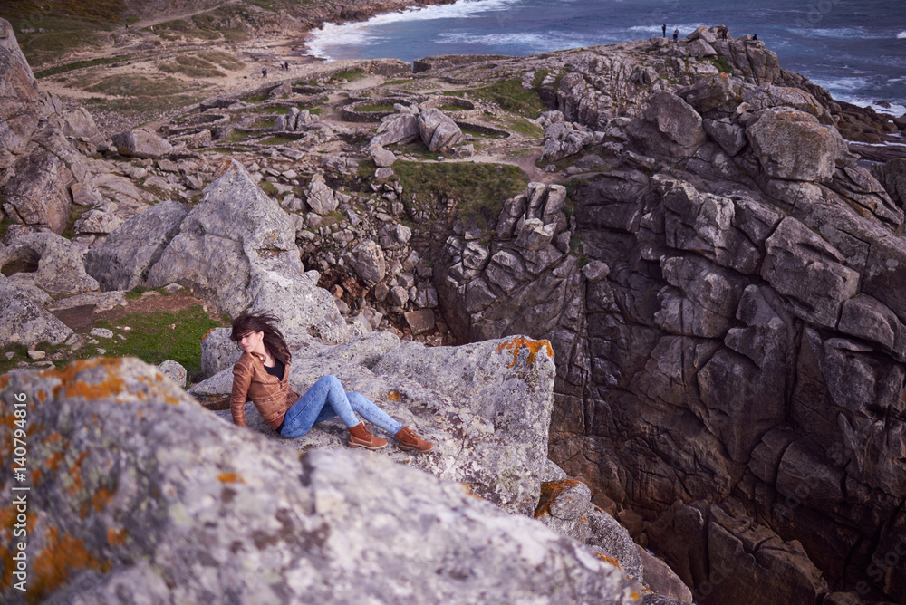 Mujer joven sentada en una roca en las ruinas del Castro de Baroña Mujer joven sentada en una roca en las ruinas del Castro de Baroña