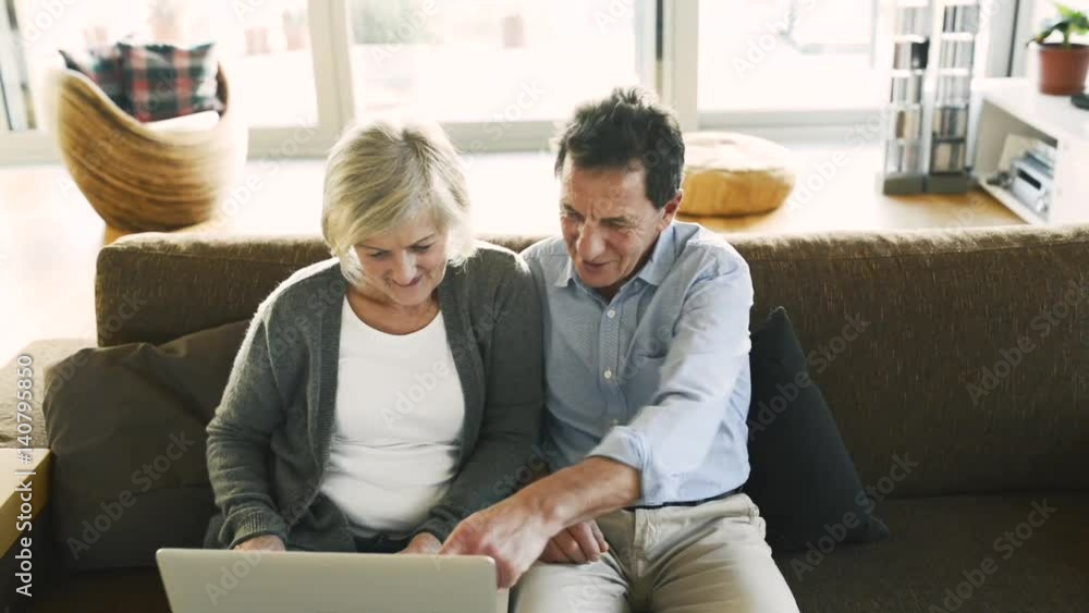 Senior couple with laptop sitting on a couch in living room Senior couple with laptop sitting on a couch in living room