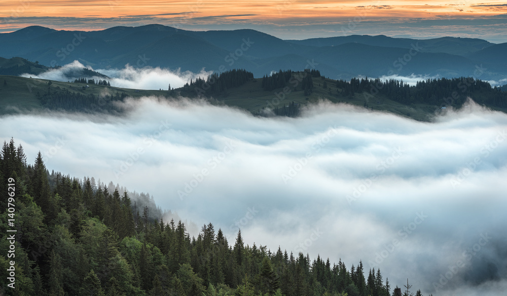 View at a mountain range with morning fog in a mountain valley. Sunrise with fog at mountains