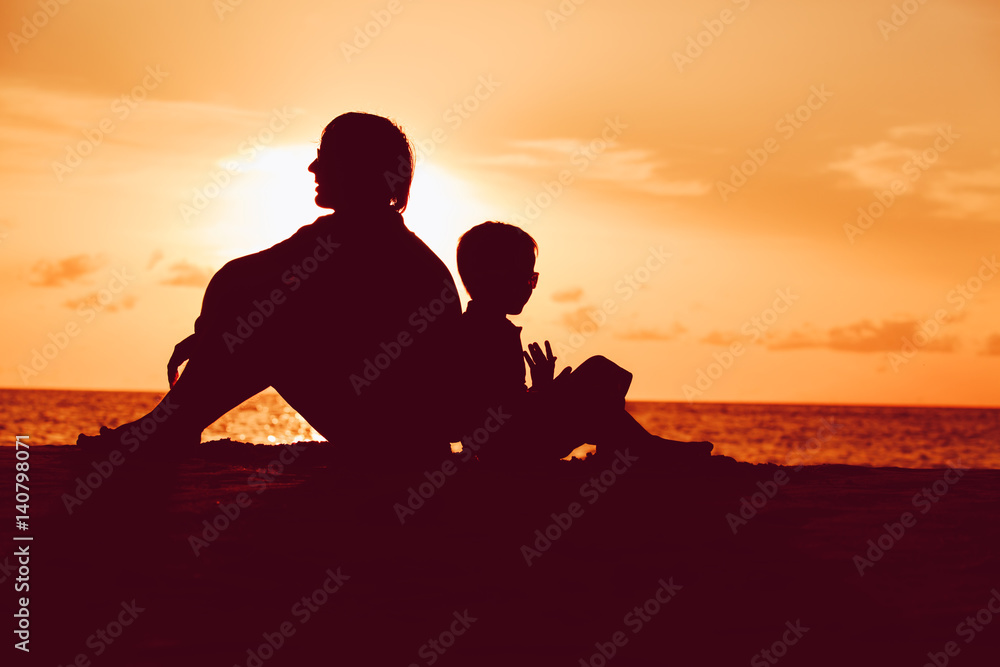 father and little son looking at sunset on beach