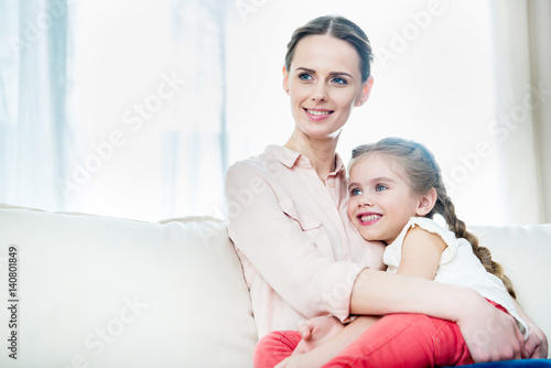 portrait of smiling daughter sitting on mother's knees at home