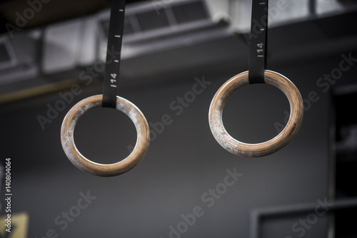 Closeup of gymnastic rings in gym with blurred athlete in background