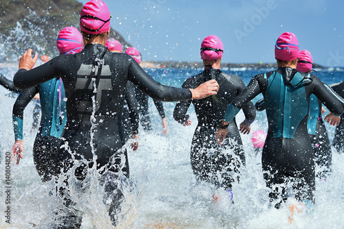 Obraz na płótnie Group triathlon participants running into the water for swim portion of race,splash of water and athletes running