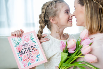 side view of smiling daughter greeting mother with tulips and postcard on mother's day