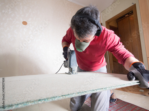 Repair in the apartment. The man cuts out the building panels. The man saws the building panel with electric jigsaw. photo