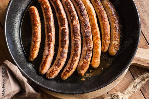 Variety of fried or roasted sausages with golden crust in iron cast pan, wood kitchen table, top view