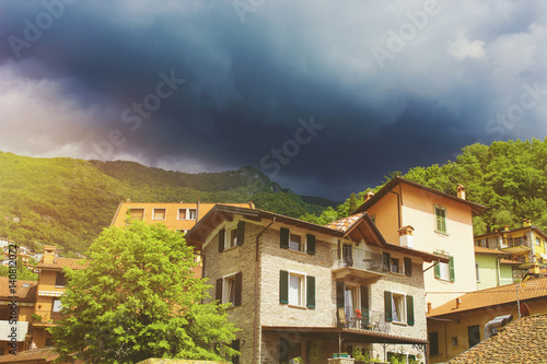 Beautiful colorful cityscape of italian Varenna city with building, green mountain and dramatic cloudy sky