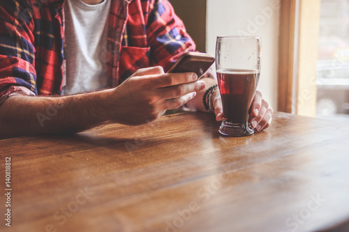 Bearded men holding beer and smartphone in bar. Close up