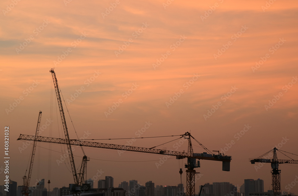Silhouette of construction cranes against evening pastel orange sky 