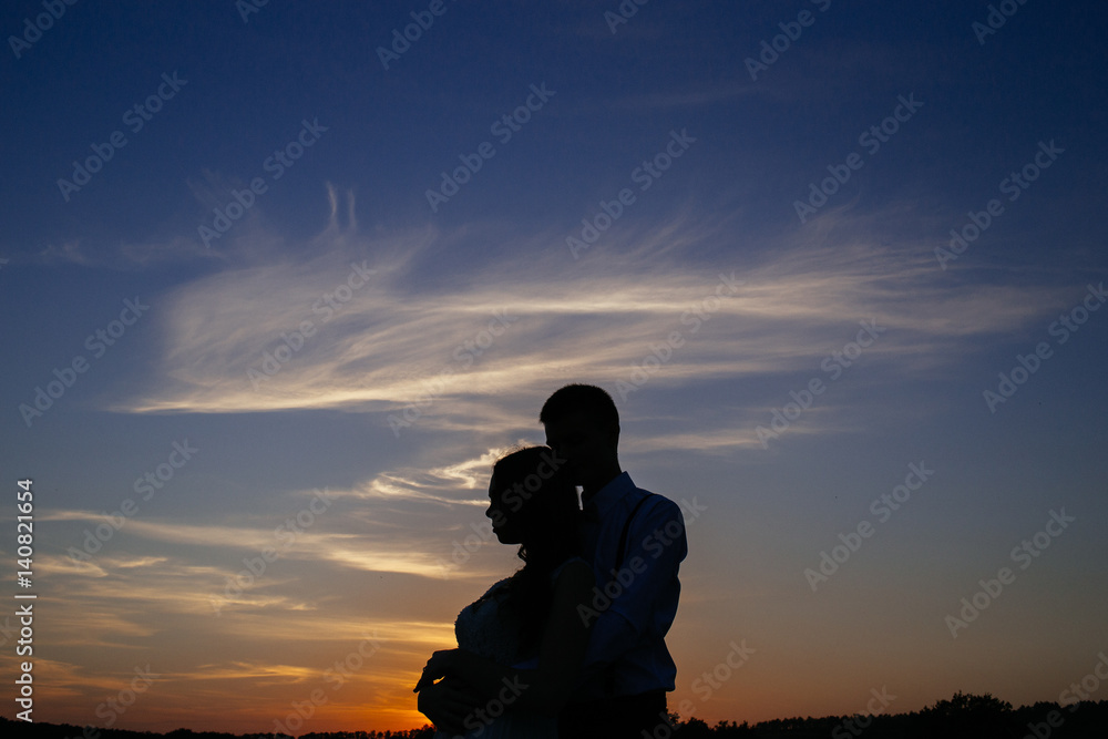 Fototapeta premium Silhouettes of a loving couple hugging at sunset