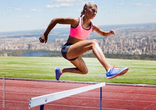Athlete running over hurdle in stadium