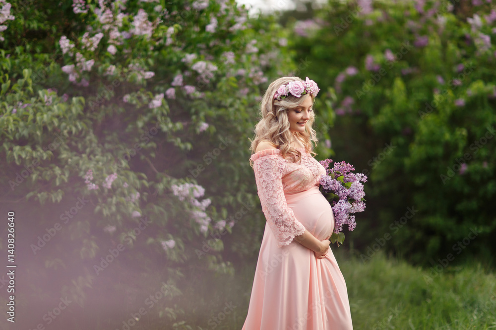 Beautiful pregnant woman with lilac bunch in spring garden