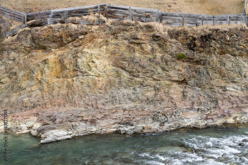 Abbruchkante mit freiliegender Felsformation in den Alpen mit Flusslauf und Zaun