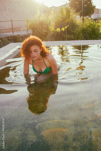 Chica joven y pelirroja dándose un baño en una piscina  photo