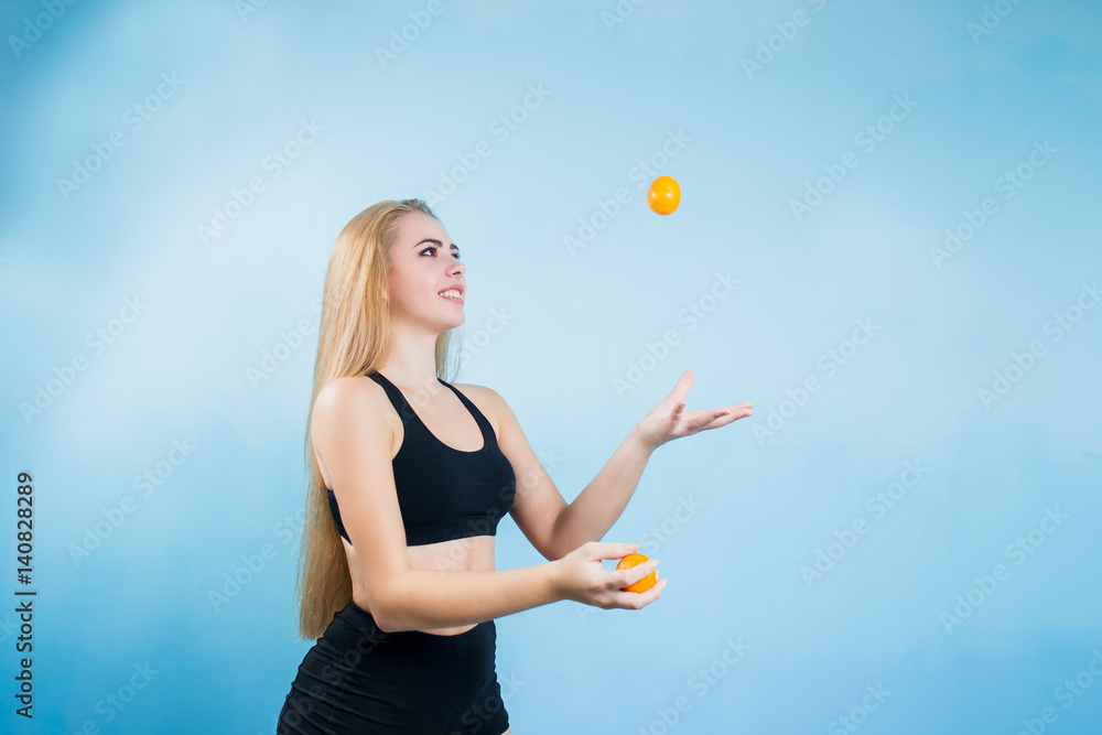 young fun, sweet and joyful girl who plays juggling with mandarins in black tracksuit shorts and